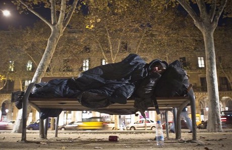 Una persona sin techo duerme en un banco junto a la Ciutadella.