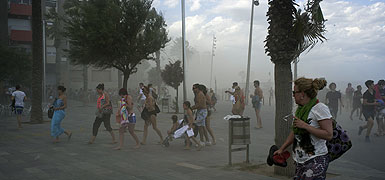 Numerosos bañistas abandonan las playas del sector de la Barceloneta, ayer a última hora de la tarde, al tiempo que intentan protegerse del impacto de la nube de arena que levanta el súbito vendaval. VICENS FORNER