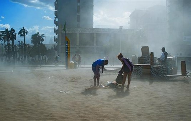 BRUMA EFÍMERA 3 Numerosos bañistas abandonan las playas del sector de la Barceloneta, ayer a última hora de la tarde, al tiempo que intentan protegerse del impacto de la nube de arena que levanta el súbito vendaval. VICENS FORNER
