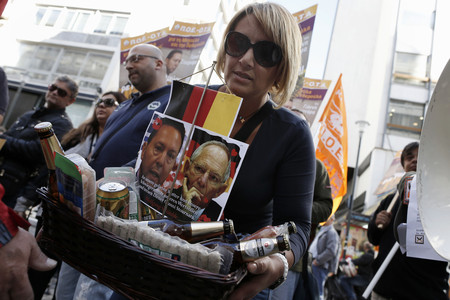 Una mujer lleva una cesta con comida y las fotos de los ministros de Finanzas griego (izquierda) y alemn, este jueves.