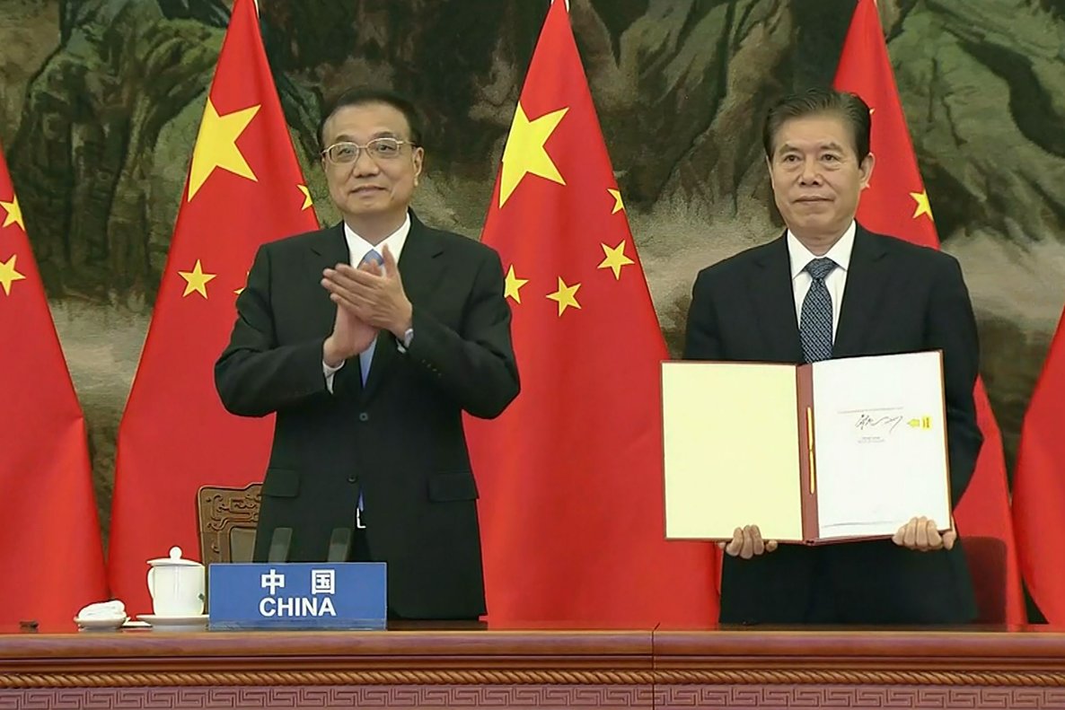 El primer ministro de China, Li Keqiang, aplaude mientras su ministro de Comercio, Zhong Shan, muestra el documento del acuerdo comercial RCEP.